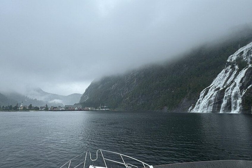 Een boot op een kalm meer met een waterval en mistige bergen op de achtergrond. 2