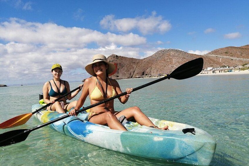 Deux personnes pratiquent le kayak par une journée ensoleillée, avec une plage et des montagnes en arrière-plan. 4