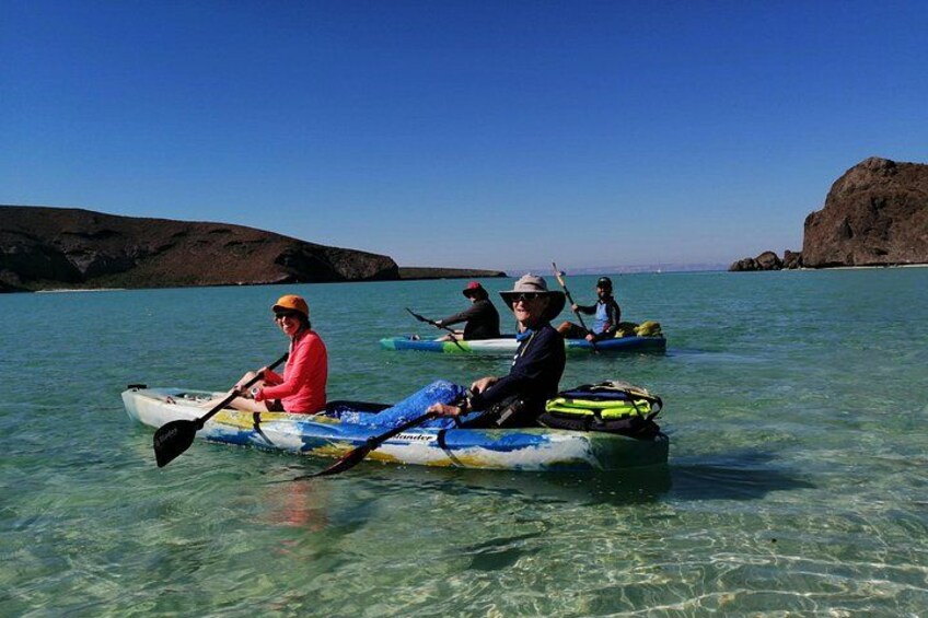 Des personnes pratiquent le kayak sur une eau claire, avec des collines rocheuses en arrière-plan. 2