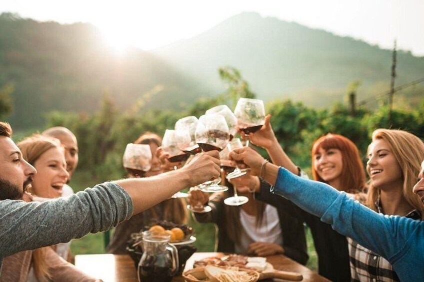 Een groep mensen die met wijn glazen proost aan een tafel met eten en een karaf. 5