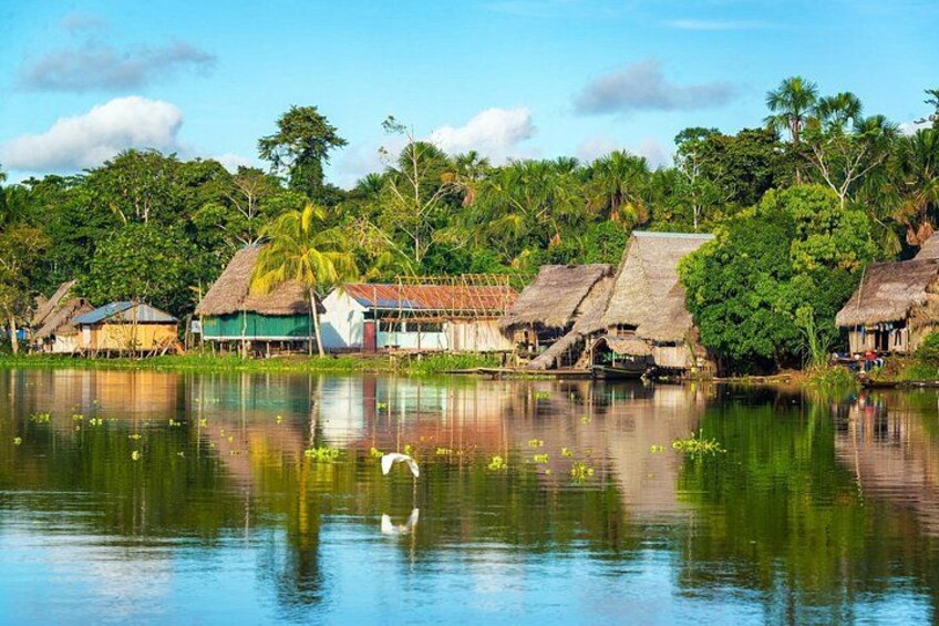 A calm lake with reflections, surrounded by thatched-roof houses and lush greenery. 1