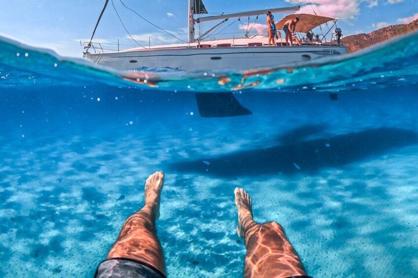 A person's legs in water with a boat and people in the background. 5