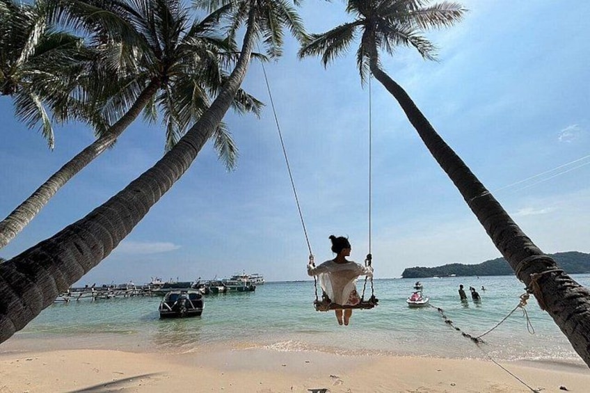 A beach with palm trees, a swing, and boats in the water. 5