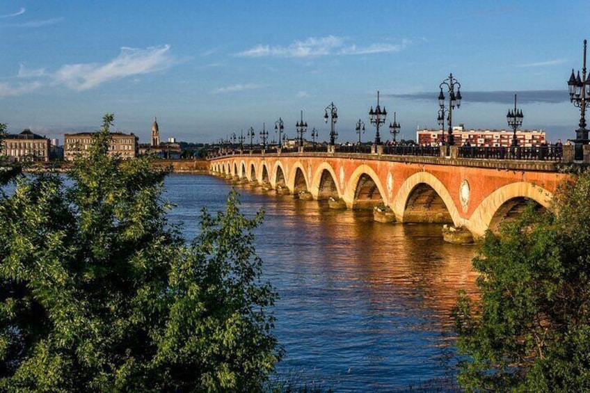 A stone bridge with arches over a river, surrounded by greenery and buildings. 4
