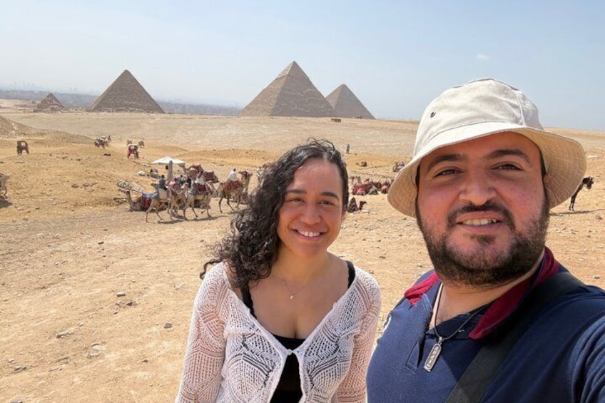 Paisaje desértico con pirámides al fondo y gente montada en camellos. 2