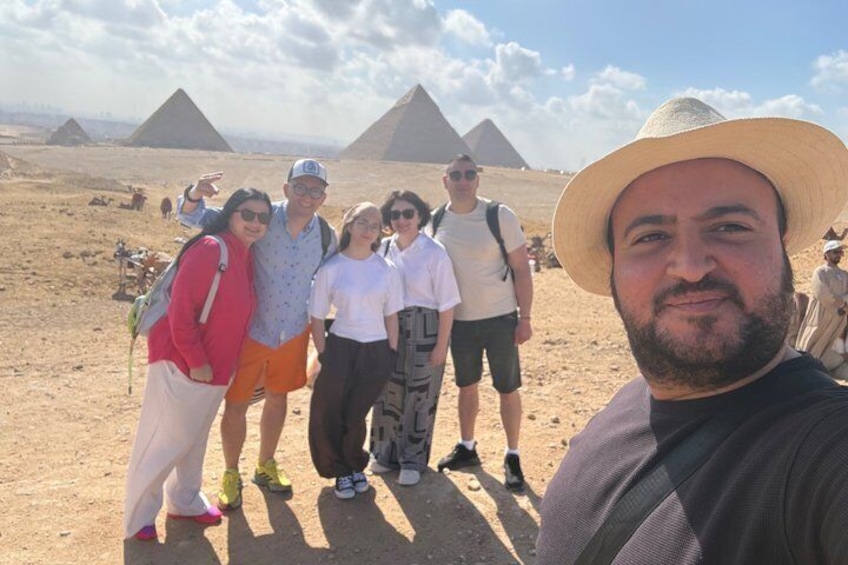 Eine Gruppe von Menschen steht in einer Wüste mit Pyramiden im Hintergrund. 1