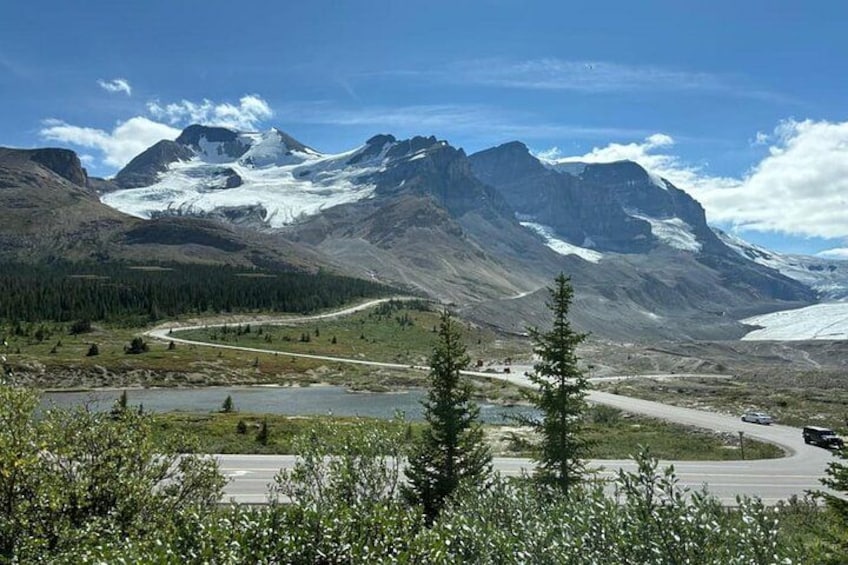 A mountainous landscape with a winding road, a lake, and snow-capped peaks. 3