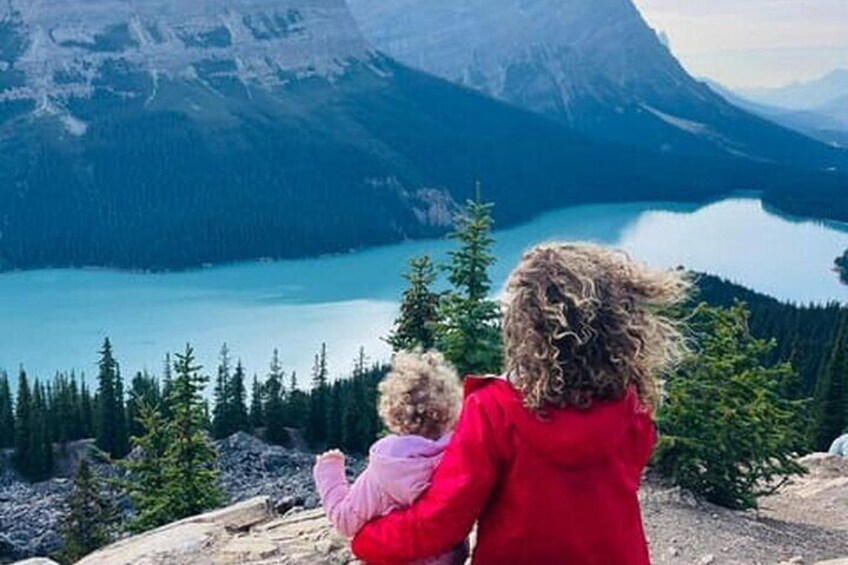 Una persona con una chaqueta roja y un niño con una chaqueta rosa observan un lago rodeado de montañas y árboles. 4