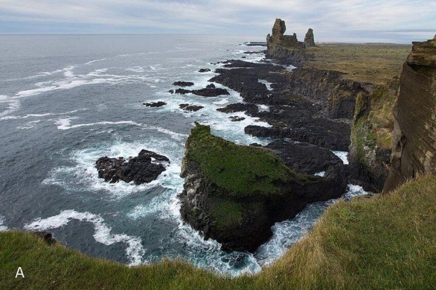 A coastal landscape with rocky cliffs, waves crashing against the shore, and a distant rocky formation. 4