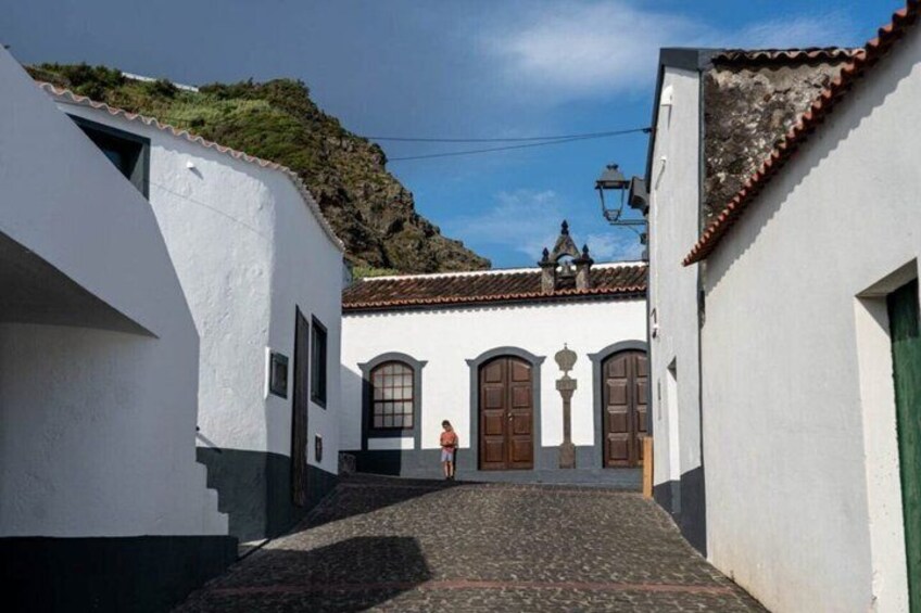 A narrow alleyway with white buildings, a person walking, and a mountain in the background. 3