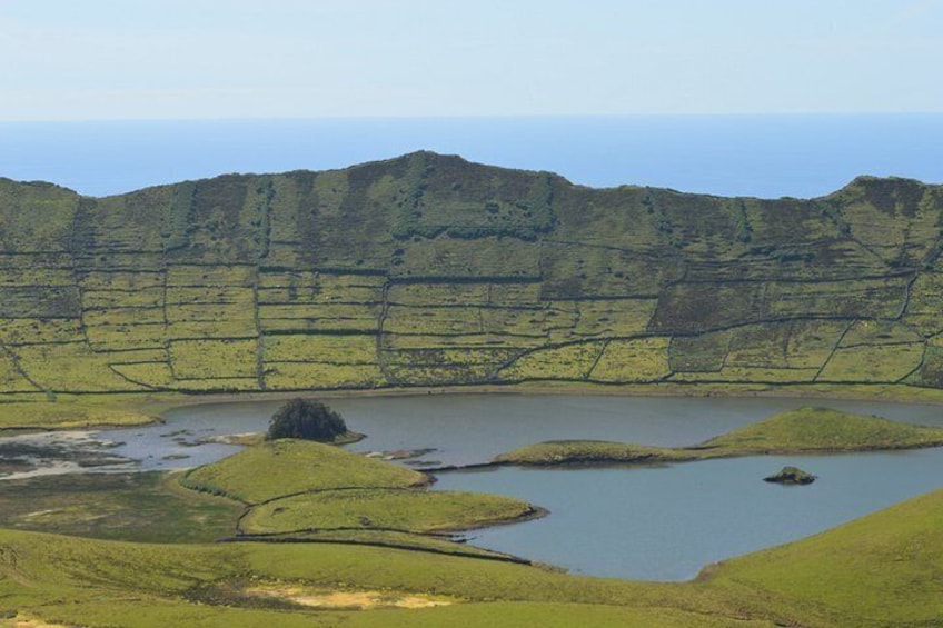 A coastal landscape with layered hills, a small lake, and a rocky outcrop. 4