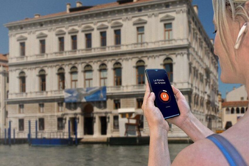 Una persona sosteniendo un teléfono inteligente con una aplicación de mapas, un edificio histórico con ventanas de arco y un cuerpo de agua al fondo. 4