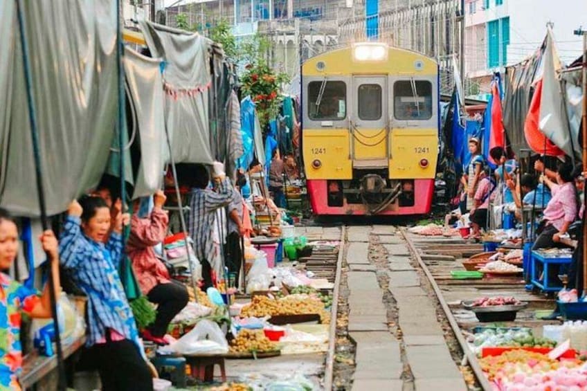 Ein Zug fährt durch einen belebten Markt mit Verkaufsständen, an denen verschiedene Waren angeboten werden. 1