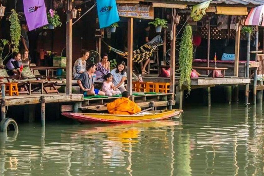 Eine Gruppe von Menschen auf einer schwimmenden Plattform, mit einer Person in einem gelben Gewand, vermutlich einem Mönch, in einem kleinen Boot. 5