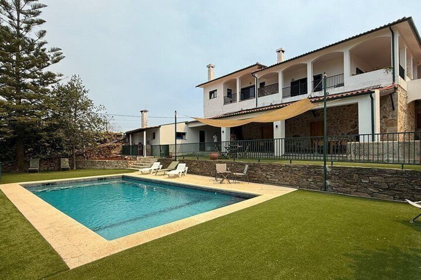 A swimming pool with a grassy area, a stone wall, and a multi-story building with balconies. 4