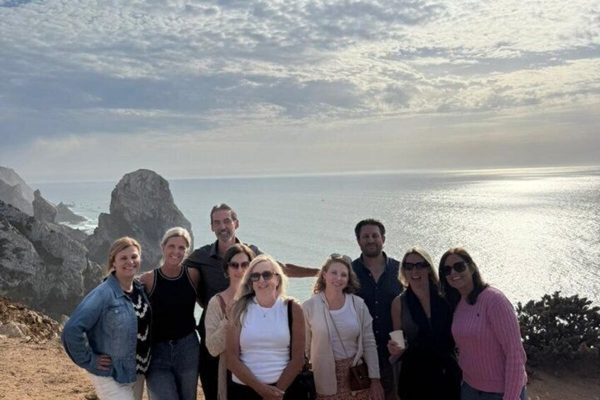 Un groupe de personnes se tient sur une falaise, surplombant un paysage côtier caractérisé par des affleurements rocheux et la mer. 4