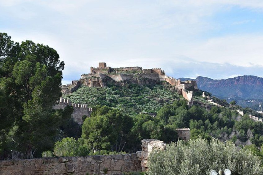 A historical fortress on a hill with surrounding greenery and a clear sky. 1