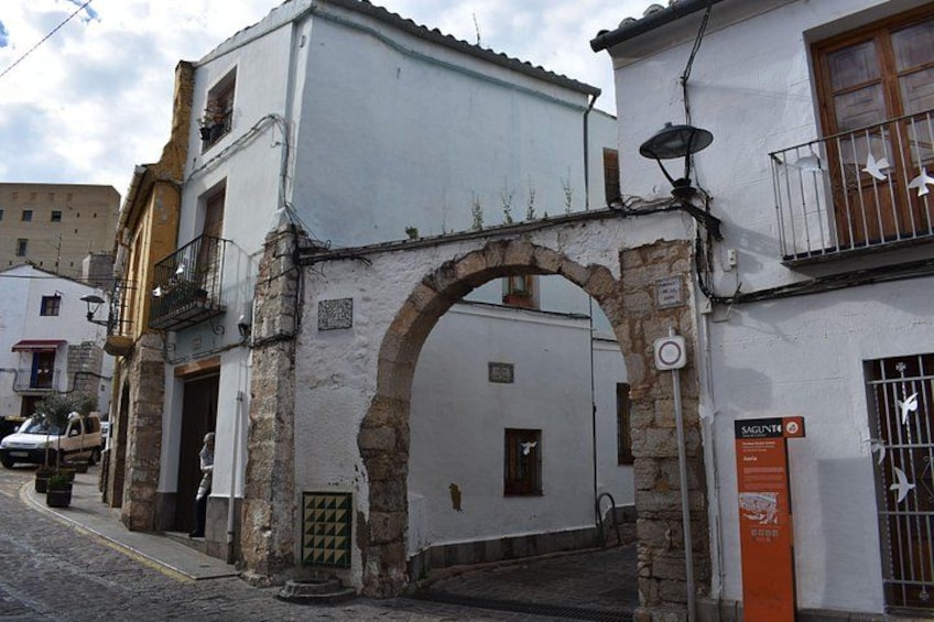 A street with a white building, an archway, and a signboard. 4