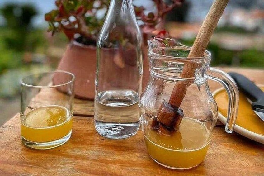 A wooden table with a glass of yellow liquid, a clear bottle, and a glass pitcher with a wooden stick. 5