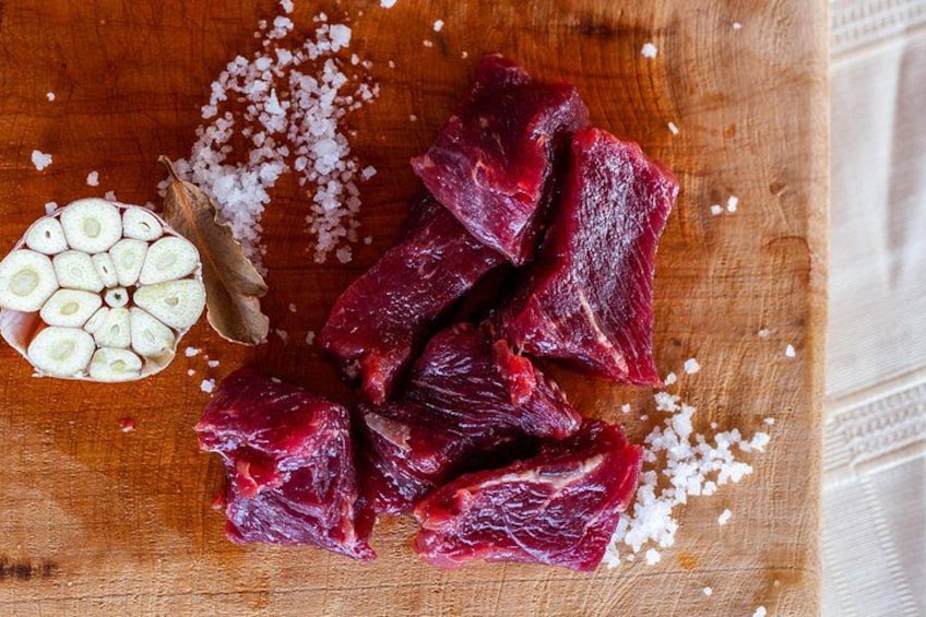 Raw beef cuts on a wooden cutting board with garlic cloves and coarse salt. 2