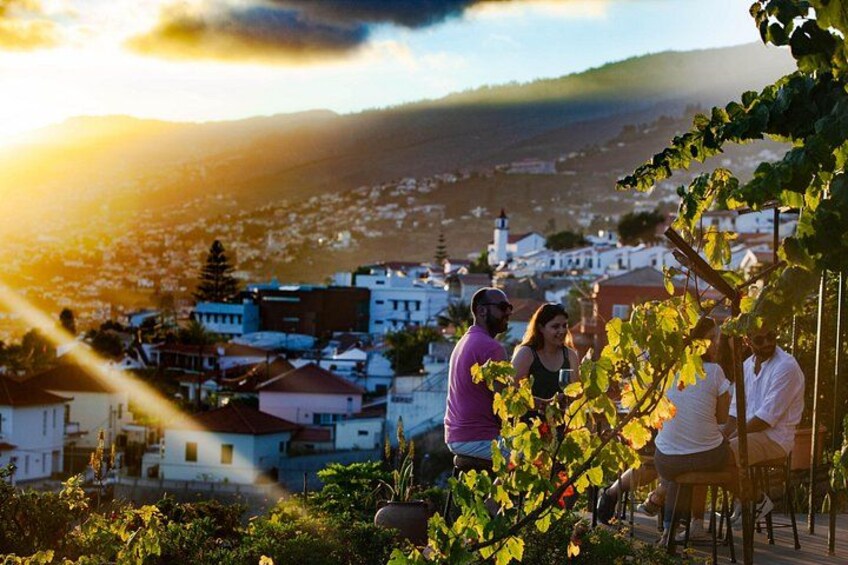 A group of people sitting on a terrace overlooking a town with white buildings and a hill in the background. 4