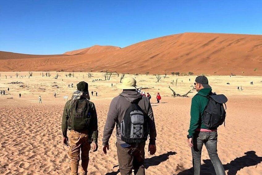 Three people walking on a sandy desert landscape with distant hills. 3