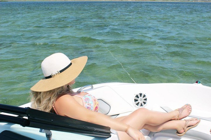A person on a boat, wearing a hat and a floral swimsuit, with water in the background. 1