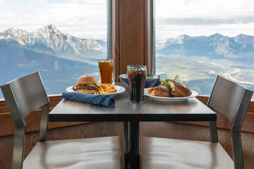 A table with two plates of food and drinks, set against a mountain backdrop. 4