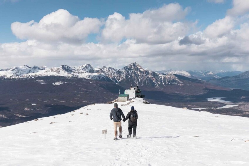 Two people walking on a snow-covered mountain with a backdrop of snow-capped peaks and a clear sky. 5