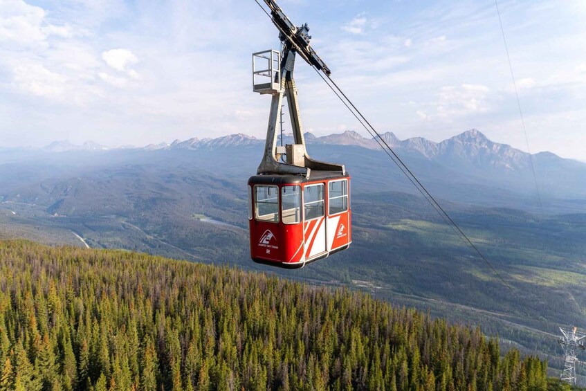 A red cable car suspended over a forested mountain landscape with distant peaks. 1
