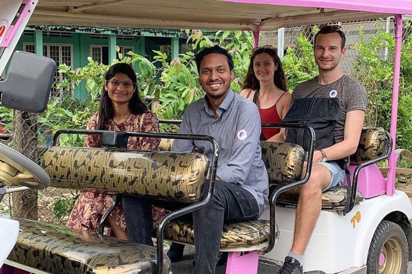 Un grupo de personas sentadas en un carrito de golf con asientos camuflados, estacionado al aire libre con follaje en el fondo. 3