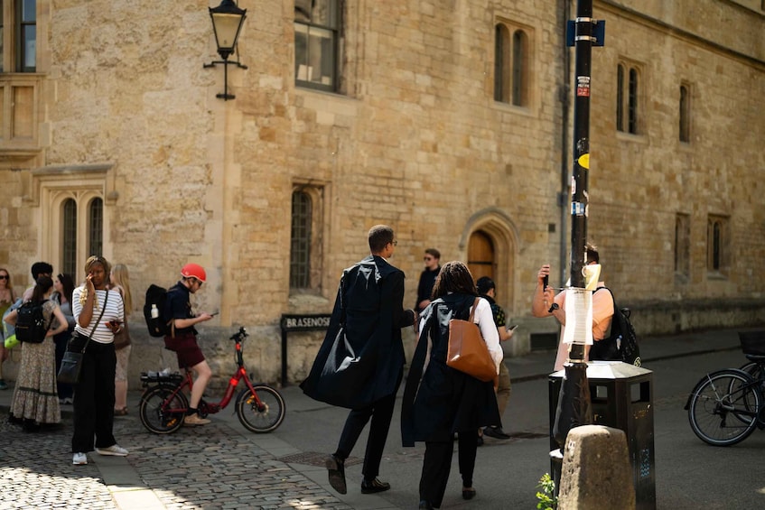 People walking on a cobblestone street, a red bicycle, and a stone building with arched windows. 5