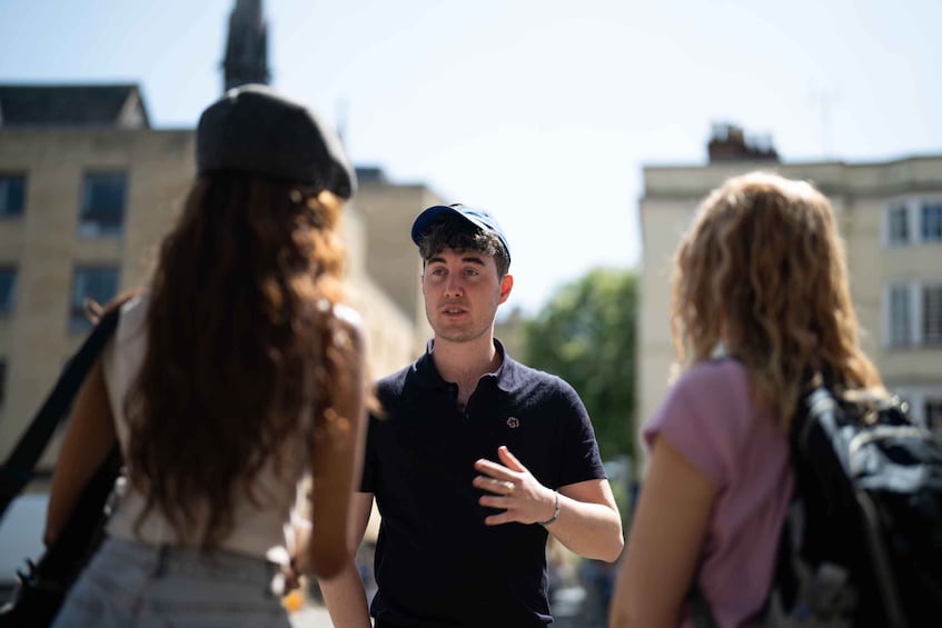 Three people conversing on a city street with buildings in the background. 1
