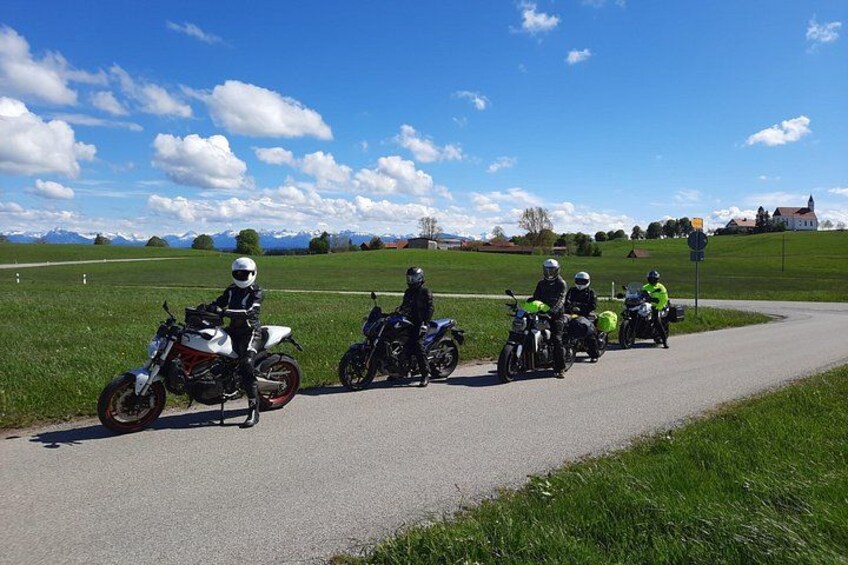A group of motorcyclists on a paved path with a rural landscape in the background. 3