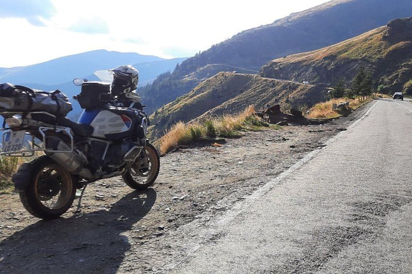 A motorcycle parked on a dirt road with mountains in the background. 1