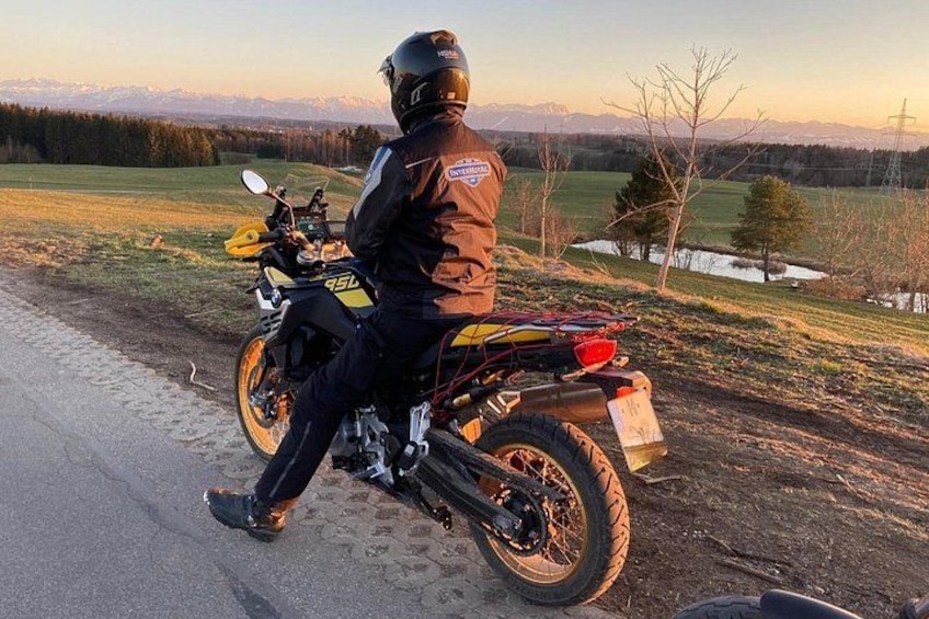 A person on a motorcycle with a helmet, riding on a paved road with a mountainous landscape in the background. 5