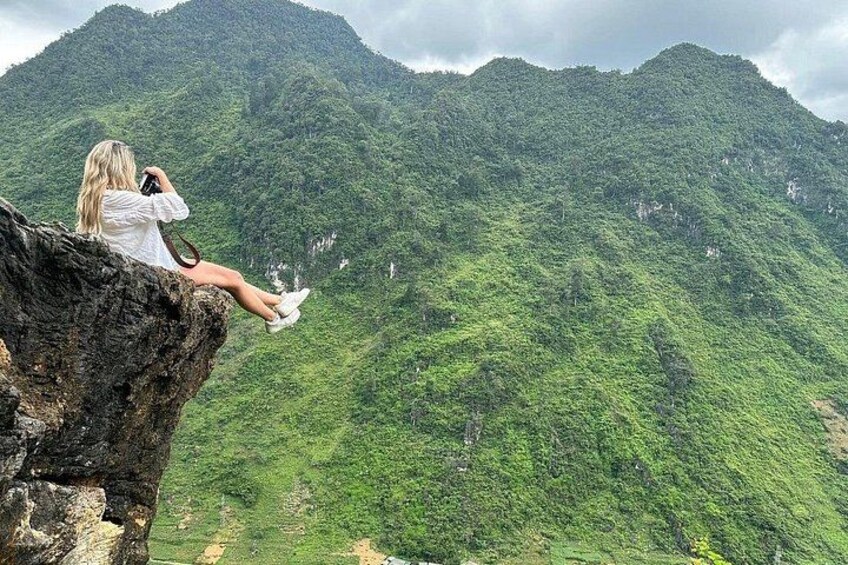 A person sitting on a rock with a mountainous landscape in the background. 4