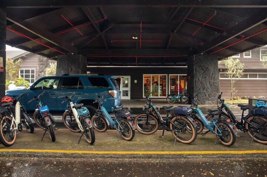 A covered parking area with several bicycles and a blue SUV. 2