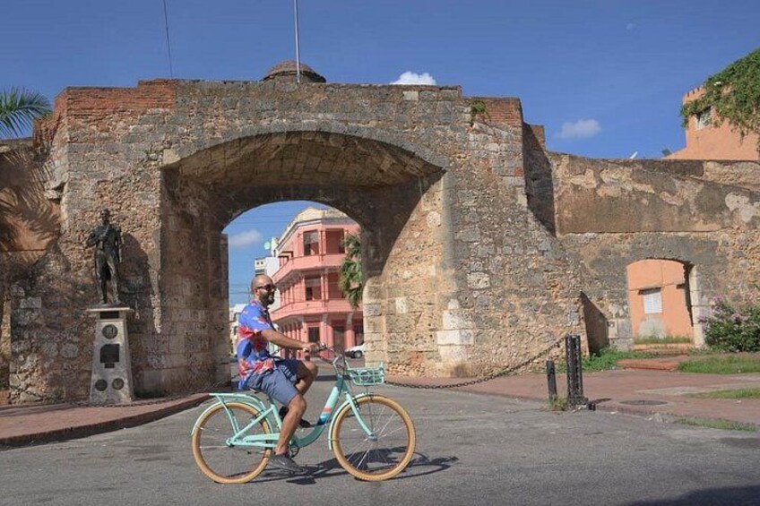 Une personne à vélo passe sous une arche en pierre, avec une statue sur le côté gauche. 1