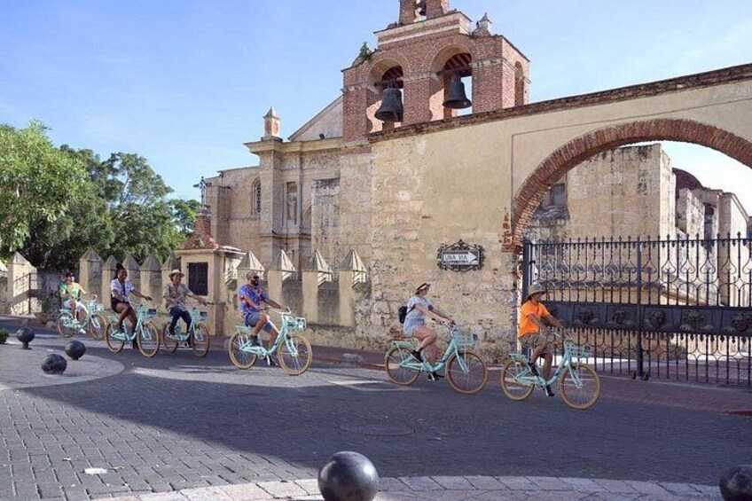 Un groupe de personnes fait du vélo dans une rue pavée, avec un bâtiment historique et une arche en arrière-plan. 4