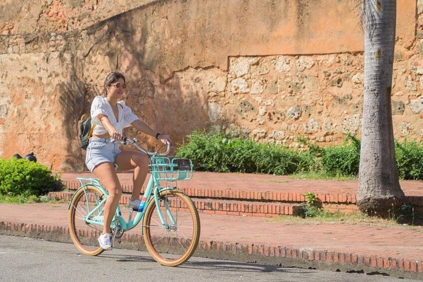 Une personne à vélo, de couleur turquoise, avec un panier, circule sur un chemin pavé. 2