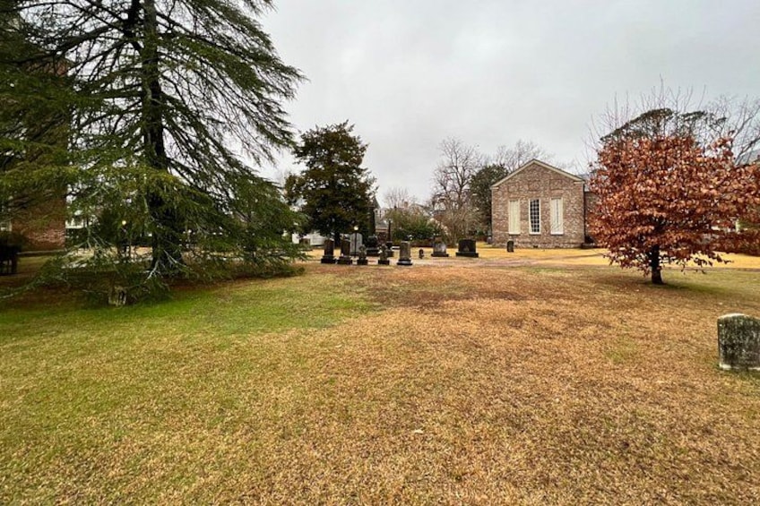 A cemetery with gravestones, a stone building, and trees. 3