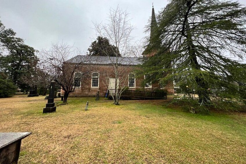 A brick building with a steeple, surrounded by trees and a grassy area. 4