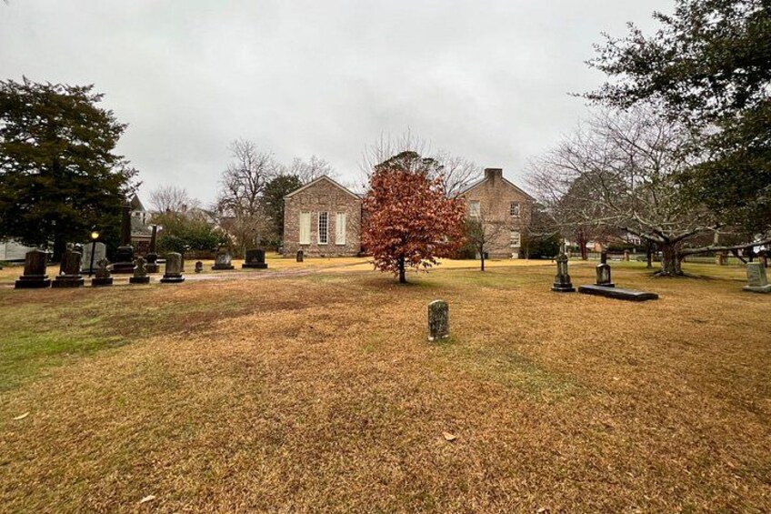 A cemetery with gravestones, a brick building, and a tree with red leaves. 2
