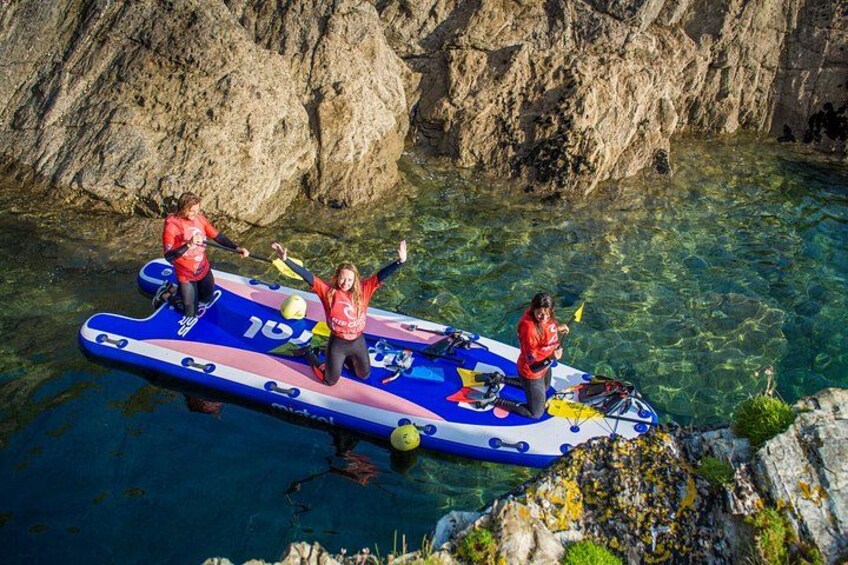 Three people on a blue inflatable raft in clear water with rocky cliffs in the background. 1