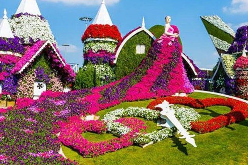 Un giardino con composizioni floreali colorate, una statua bianca e una donna con un abito rosa. 1
