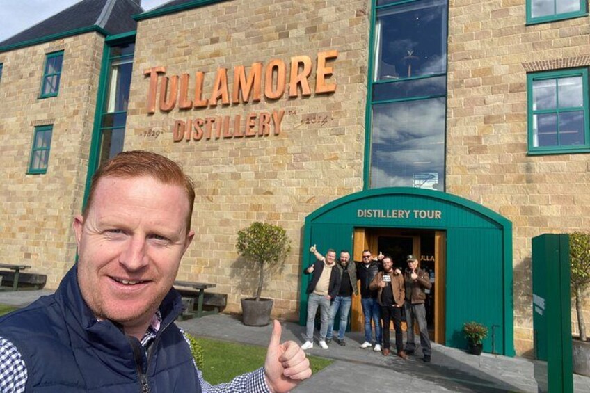 A building with a sign that reads 'Tullamore Distillery' and a group of people standing at the entrance. 1