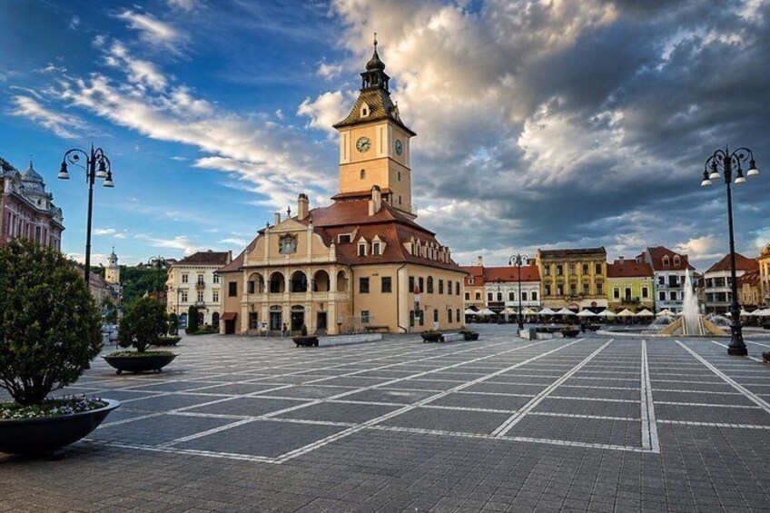 Una piazza storica con un'imponente torre dell'orologio, circondata da edifici tradizionali e una pavimentazione a lastriche. 3