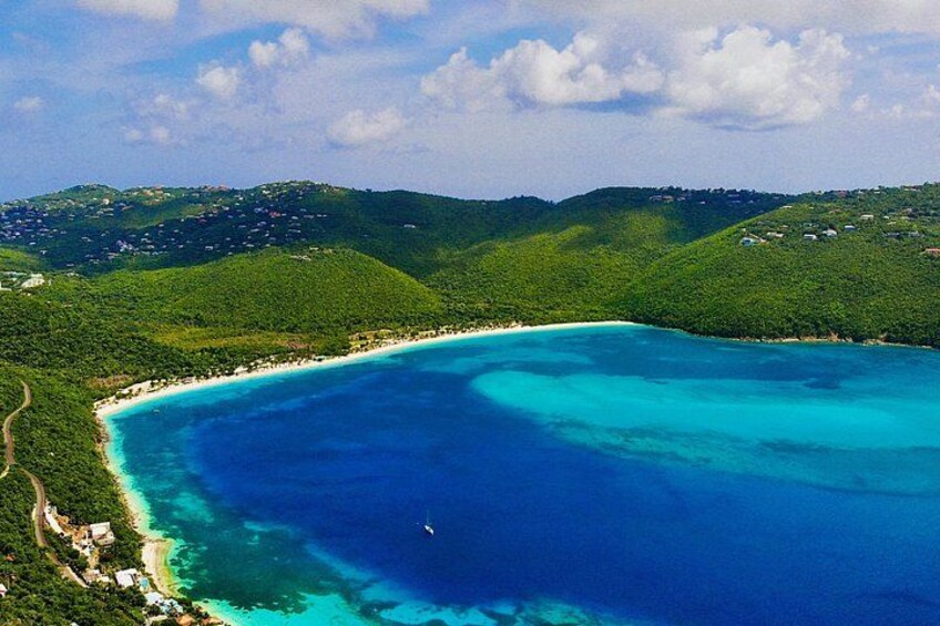 A coastal landscape with a turquoise bay, green hills, and a clear sky. 1
