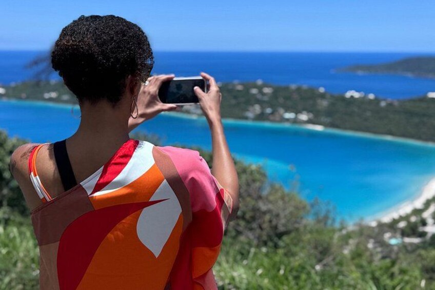 A person taking a photo of a coastal landscape with clear blue waters and a distant island. 5